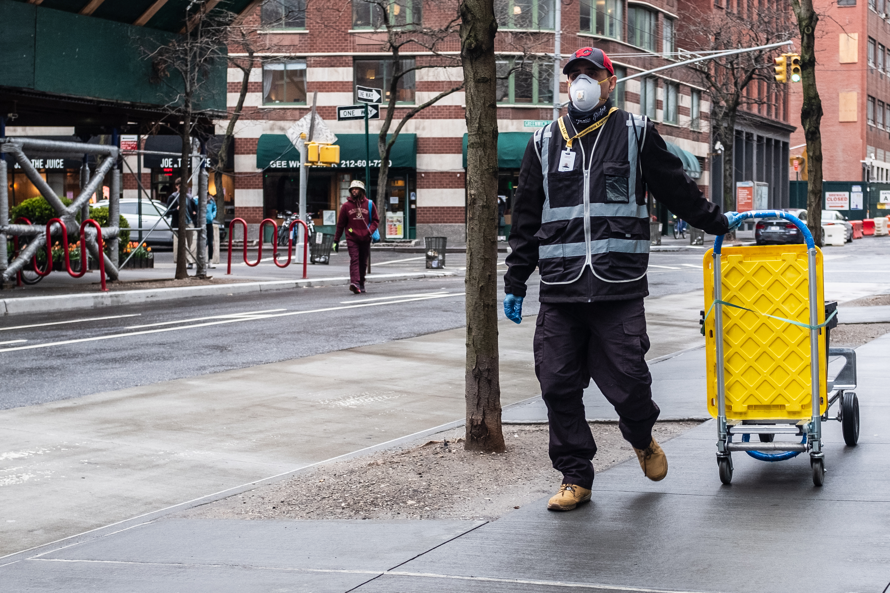 Man wearing a face mask pulls a cart while walking on the sidewalk in New York.